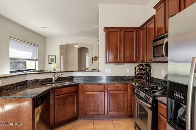 kitchen featuring dark stone counters, a sink, arched walkways, and appliances with stainless steel finishes