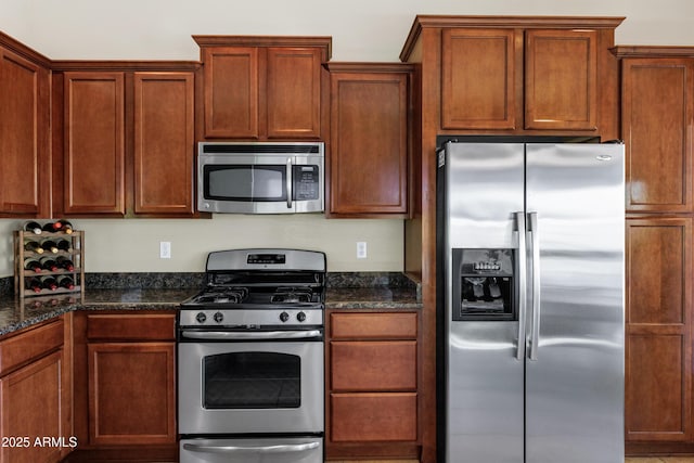 kitchen with brown cabinetry, dark stone countertops, and appliances with stainless steel finishes
