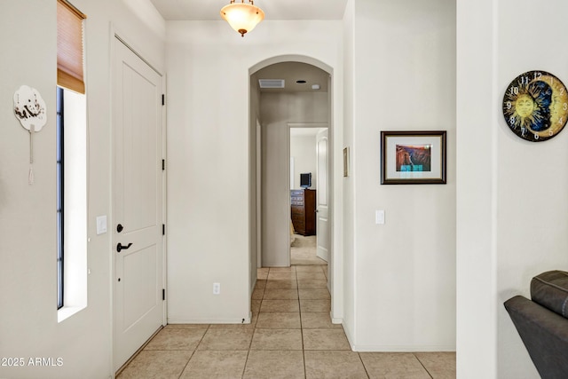 hallway featuring arched walkways, baseboards, visible vents, and light tile patterned floors