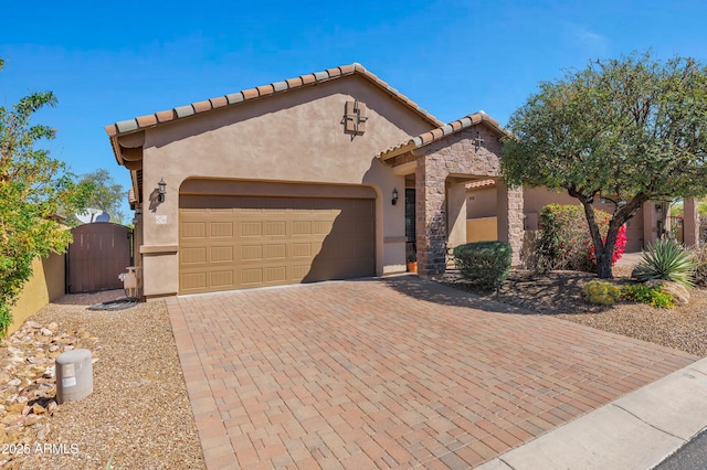 mediterranean / spanish house featuring stucco siding, an attached garage, stone siding, decorative driveway, and a gate