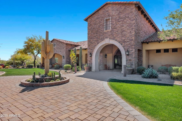 mediterranean / spanish-style house featuring stone siding, a tile roof, a front lawn, and stucco siding
