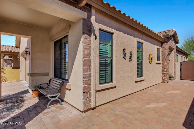 view of home's exterior with stucco siding, a gate, a tile roof, and a patio