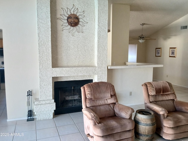 living area with vaulted ceiling, a textured ceiling, light tile patterned floors, ceiling fan, and a fireplace