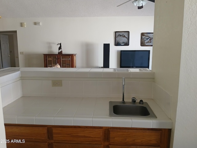 kitchen with ceiling fan, sink, tile counters, and a textured ceiling