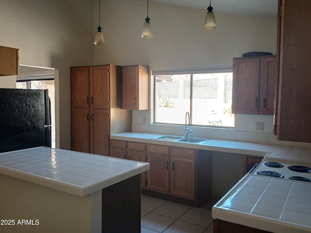 kitchen with pendant lighting, sink, light tile patterned floors, black refrigerator, and tile countertops