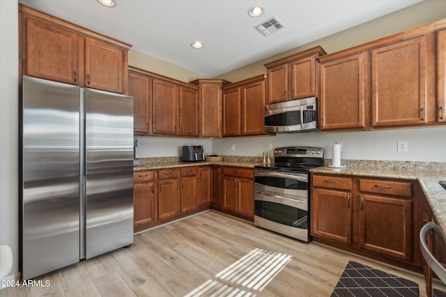 kitchen featuring light stone countertops, appliances with stainless steel finishes, and light wood-type flooring