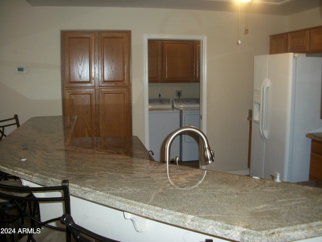 kitchen with washer and clothes dryer, a kitchen breakfast bar, and white refrigerator with ice dispenser