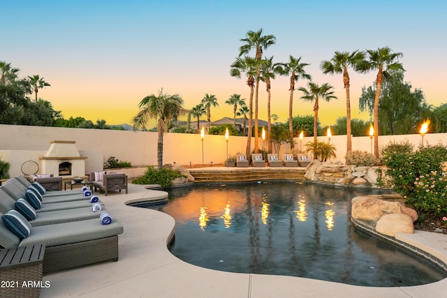 pool at dusk featuring exterior fireplace and a patio area