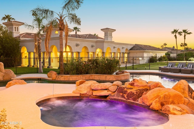 pool at dusk featuring an in ground hot tub and pool water feature