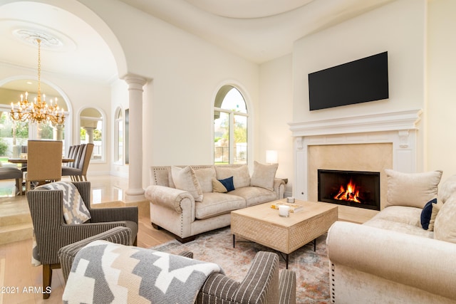 living room featuring an inviting chandelier, light wood-type flooring, a premium fireplace, and ornate columns