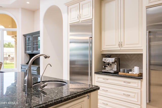 kitchen featuring high quality fridge, tasteful backsplash, stainless steel built in refrigerator, sink, and dark stone countertops