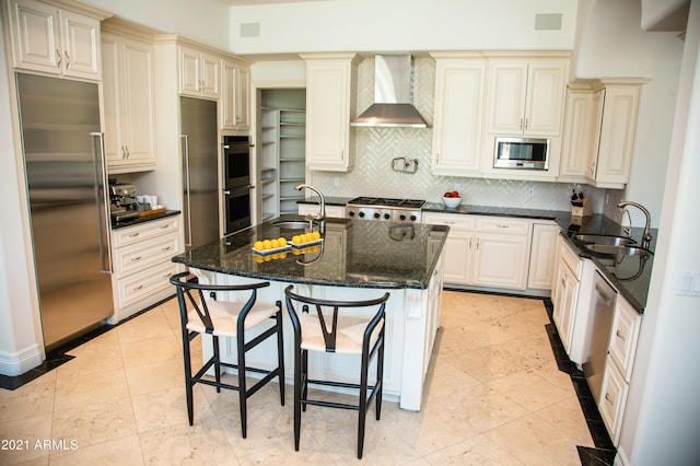 kitchen with built in appliances, wall chimney range hood, sink, and dark stone countertops