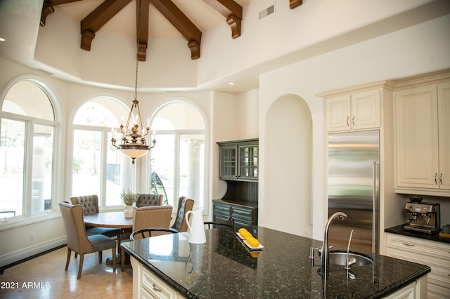 kitchen featuring stainless steel built in refrigerator, beam ceiling, sink, and dark stone countertops