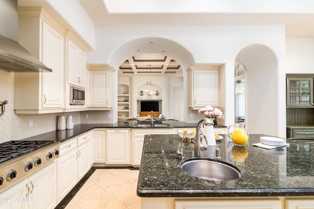 kitchen featuring wall chimney exhaust hood, coffered ceiling, sink, dark stone counters, and beam ceiling