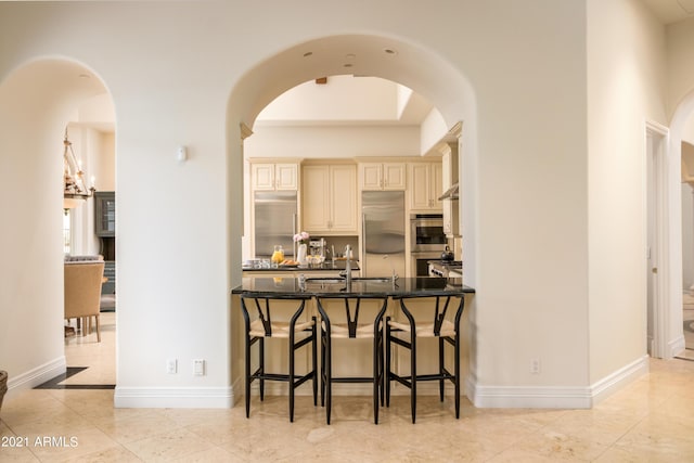 kitchen with sink, light tile patterned floors, dark stone counters, stainless steel appliances, and cream cabinetry