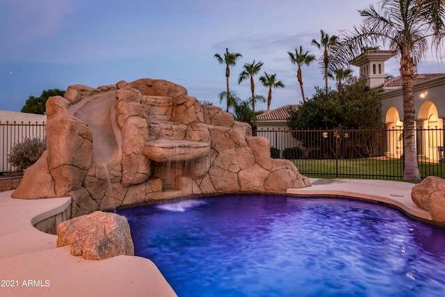 pool at dusk featuring pool water feature