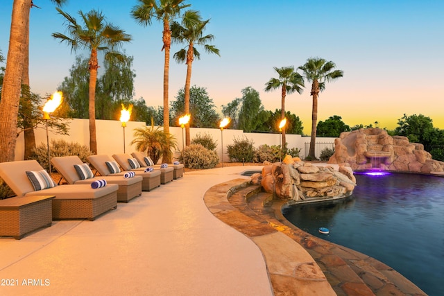 pool at dusk with pool water feature and a patio area