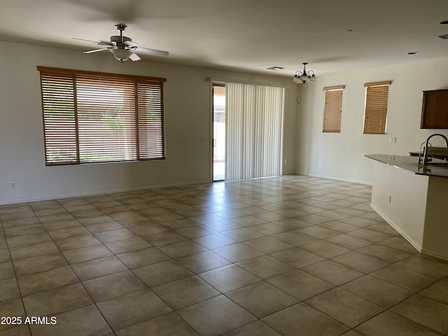 unfurnished living room featuring tile patterned flooring, baseboards, a sink, and ceiling fan with notable chandelier