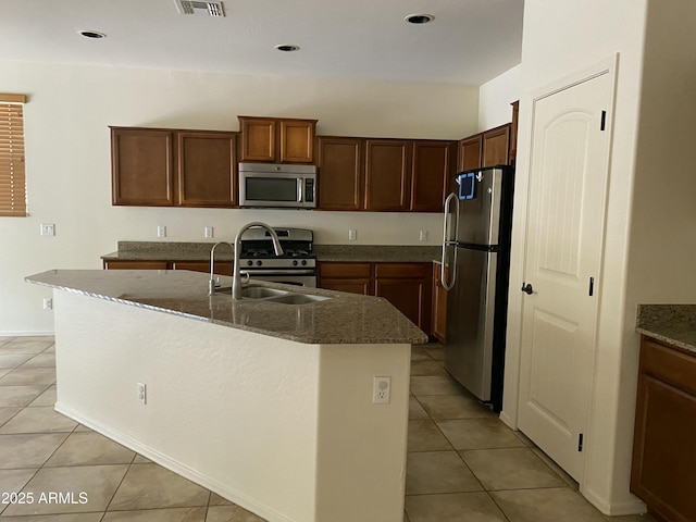 kitchen featuring appliances with stainless steel finishes, dark stone counters, a sink, and light tile patterned floors