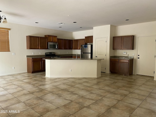 kitchen with baseboards, visible vents, dark countertops, an island with sink, and stainless steel appliances