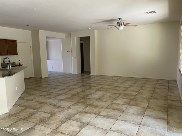 unfurnished living room with light tile patterned floors, baseboards, visible vents, a ceiling fan, and a sink