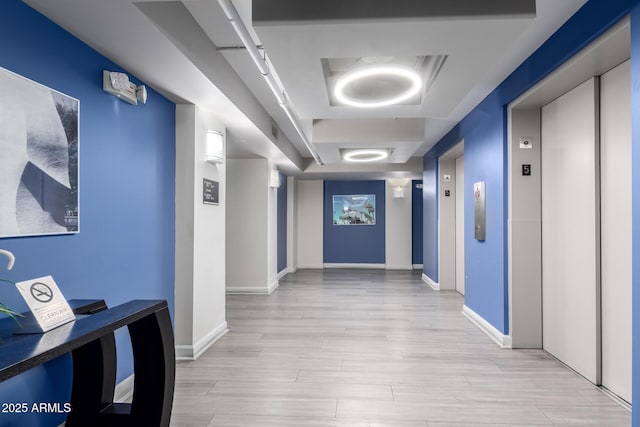 hall featuring light hardwood / wood-style flooring, a raised ceiling, and elevator