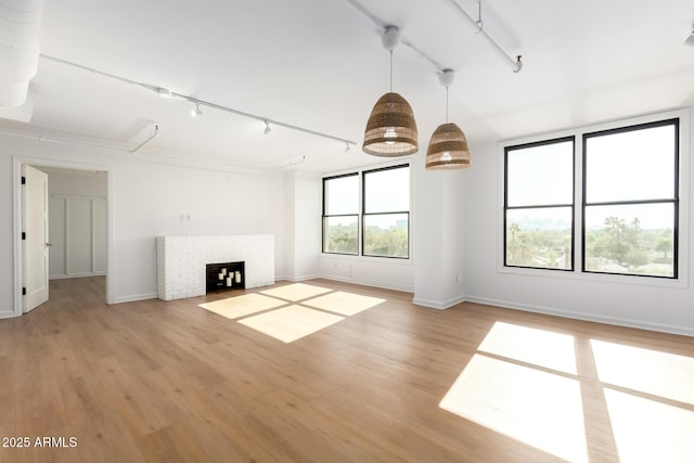 unfurnished living room with a brick fireplace, rail lighting, and light hardwood / wood-style floors