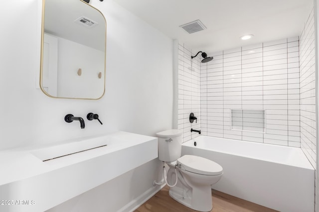 bathroom featuring toilet, tiled shower / bath combo, and wood-type flooring