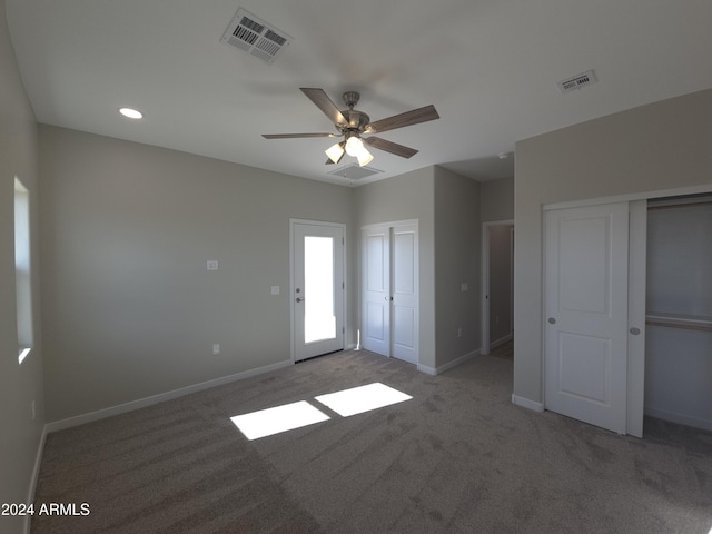 unfurnished bedroom with multiple closets, light colored carpet, and ceiling fan