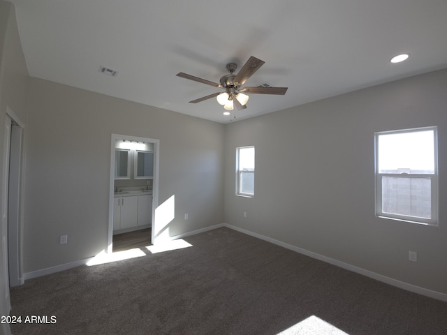 unfurnished bedroom with ensuite bathroom, ceiling fan, and dark carpet