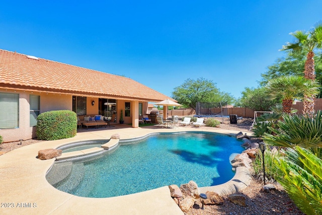 view of swimming pool with a trampoline, a pool with connected hot tub, a patio area, and a fenced backyard