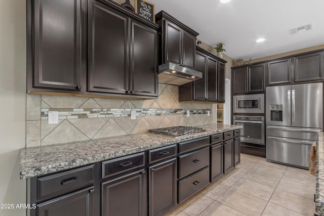 kitchen featuring appliances with stainless steel finishes, under cabinet range hood, backsplash, light stone countertops, and light tile patterned floors