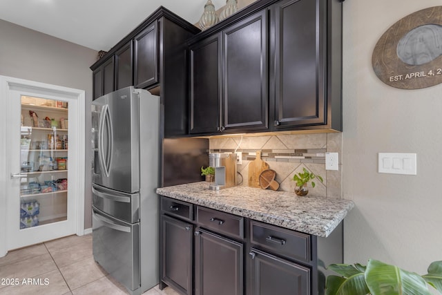 kitchen featuring stainless steel fridge, backsplash, light stone counters, and light tile patterned flooring