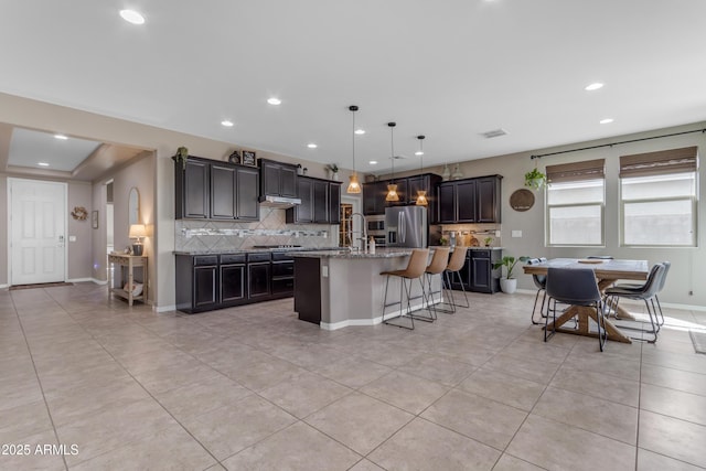 kitchen with stainless steel appliances, backsplash, recessed lighting, a kitchen breakfast bar, and a kitchen island with sink