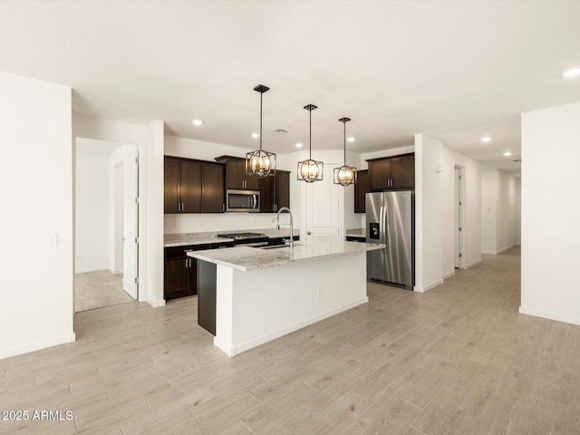 kitchen with recessed lighting, dark brown cabinets, light wood-style floors, stainless steel appliances, and a kitchen island with sink