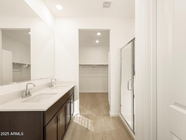 full bath featuring a stall shower, a spacious closet, visible vents, and a sink