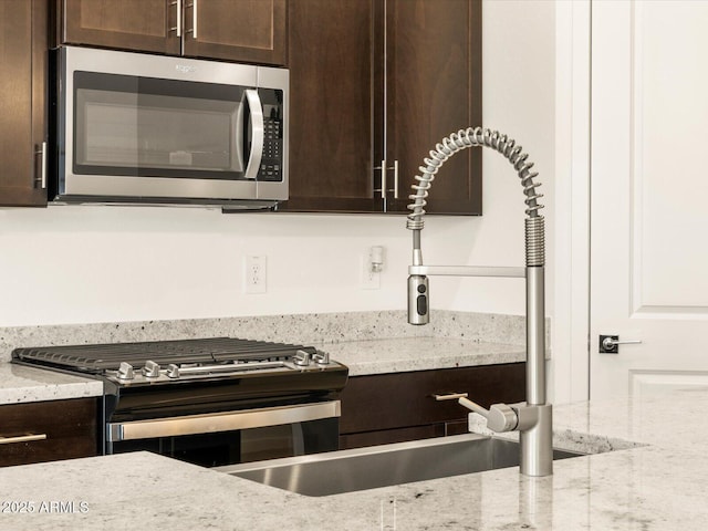 kitchen featuring appliances with stainless steel finishes, dark brown cabinets, and light stone countertops