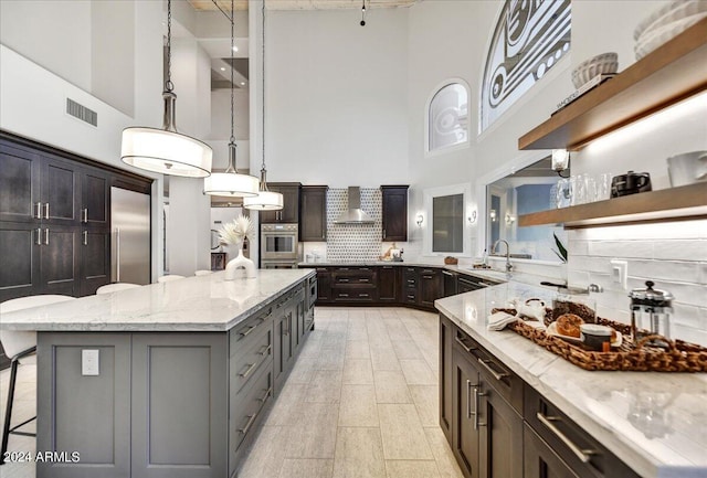 kitchen featuring backsplash, wall chimney exhaust hood, high quality fridge, decorative light fixtures, and a kitchen island