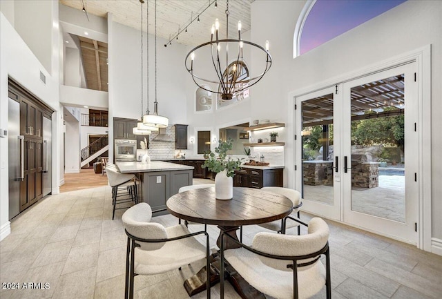 dining space featuring an inviting chandelier, light wood-type flooring, a towering ceiling, and french doors