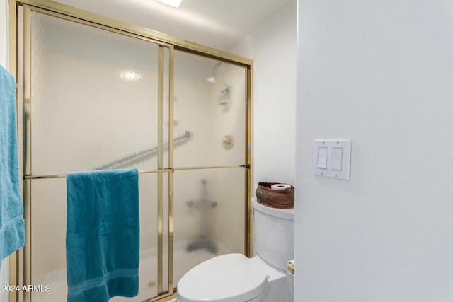 bathroom featuring a shower with door and toilet