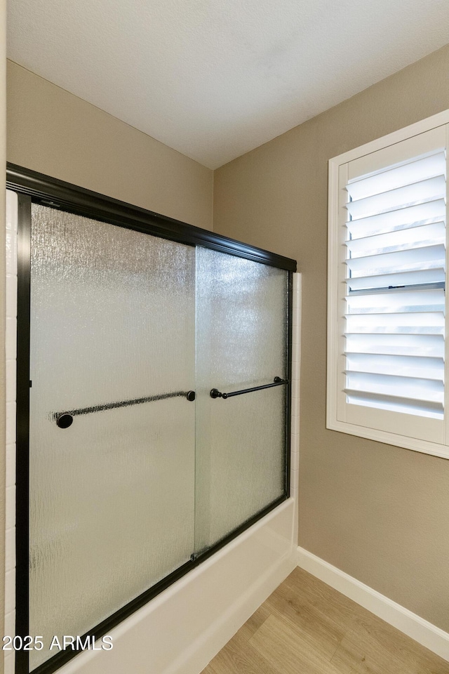 bathroom featuring hardwood / wood-style flooring and shower / bath combination with glass door