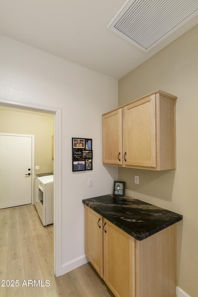 kitchen featuring dark stone countertops, washer / clothes dryer, light hardwood / wood-style floors, and light brown cabinets