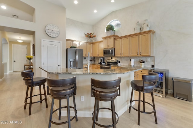 kitchen with wine cooler, light brown cabinets, stainless steel appliances, light hardwood / wood-style floors, and a high ceiling