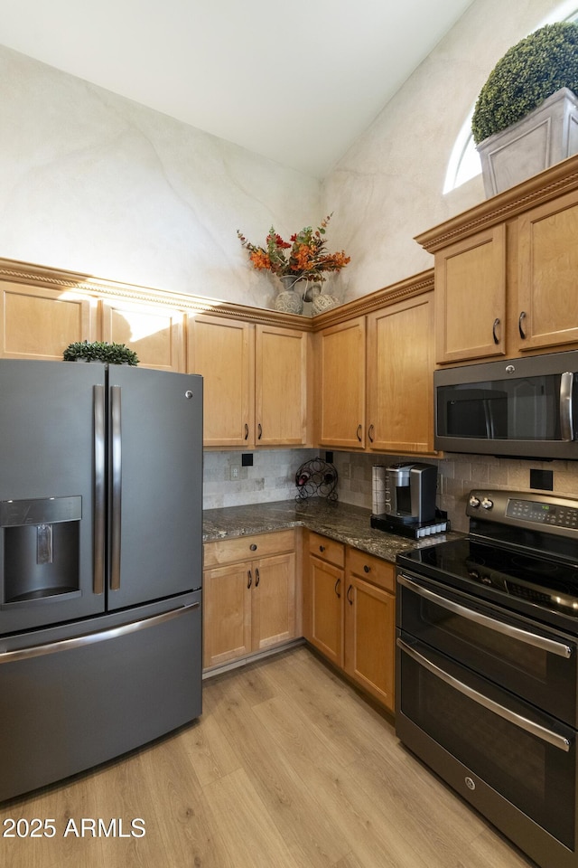 kitchen with tasteful backsplash, appliances with stainless steel finishes, light hardwood / wood-style flooring, and dark stone countertops