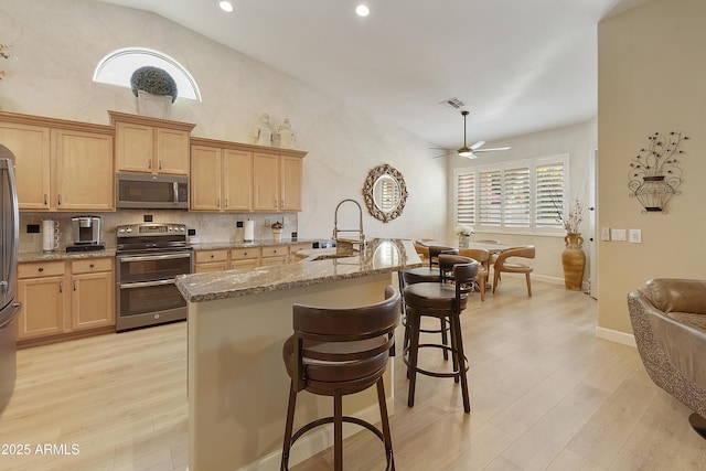 kitchen featuring stainless steel appliances, a kitchen breakfast bar, light stone counters, and light hardwood / wood-style flooring