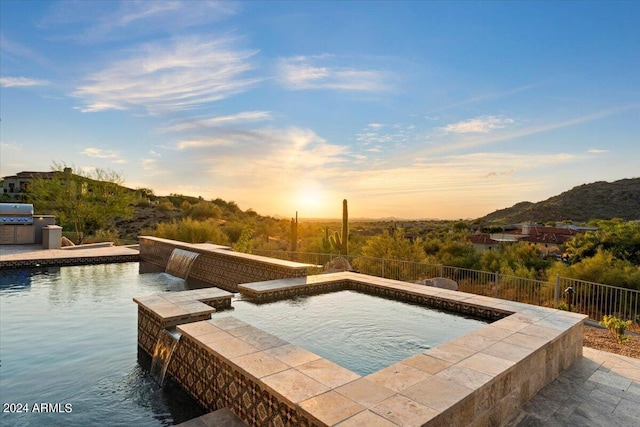 pool at dusk featuring a mountain view, area for grilling, and pool water feature