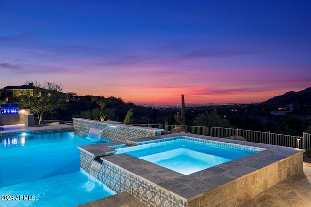 pool at dusk featuring an in ground hot tub and pool water feature