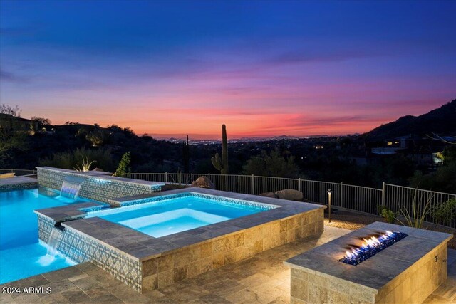 pool at dusk featuring a fire pit, an in ground hot tub, and pool water feature