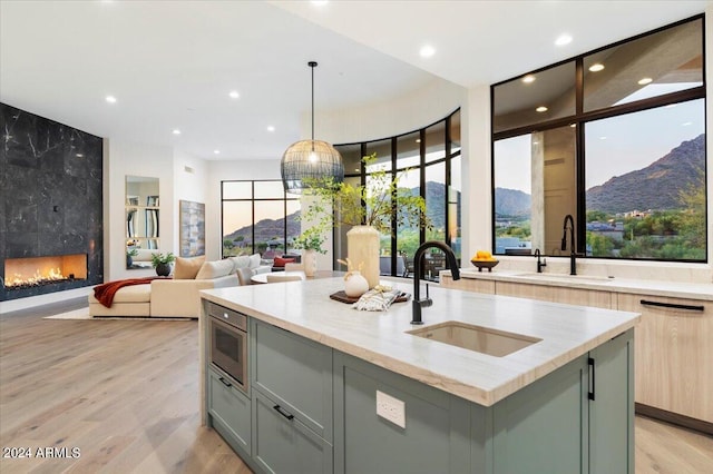 kitchen with light wood-type flooring, a high end fireplace, a mountain view, hanging light fixtures, and a center island with sink