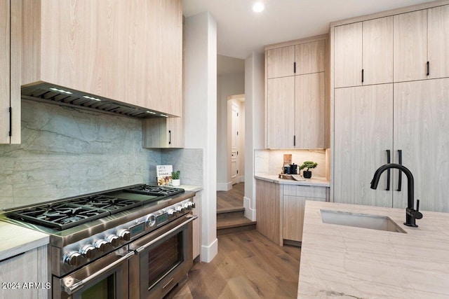 kitchen featuring light brown cabinetry, light wood-type flooring, sink, wall chimney exhaust hood, and double oven range